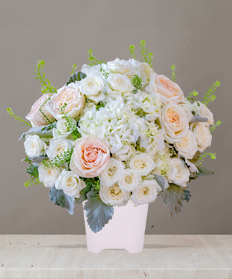 Billy Heroman's Signature Collection white and blush flower arrangement with roses, hydrangeas, and greenery in a textured white vase