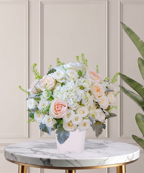 Billy Heroman's Signature Collection white and blush flower arrangement with roses, hydrangeas, and greenery in a textured white vase