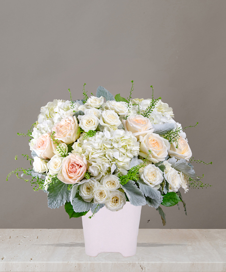 Billy Heroman's Signature Collection white and blush flower arrangement with roses, hydrangeas, and greenery in a textured white vase