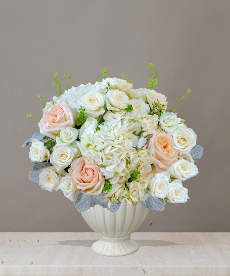 Billy Heroman's Signature Collection white and blush flower arrangement with roses, hydrangeas, and greenery in a textured white vase