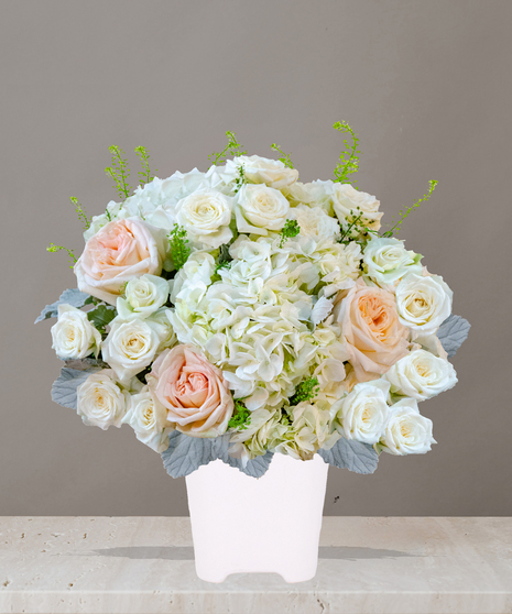 Billy Heroman's Signature Collection white and blush flower arrangement with roses, hydrangeas, and greenery in a textured white vase