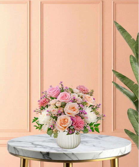 Peepin’ Pretty floral arrangement with blush and fuchsia roses, carnations, ivory mums, and lavender asters in a white ceramic vase.