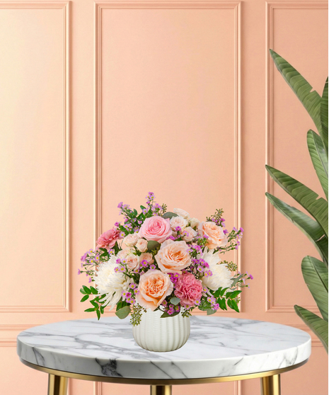 Peepin’ Pretty floral arrangement with blush and fuchsia roses, carnations, ivory mums, and lavender asters in a white ceramic vase.