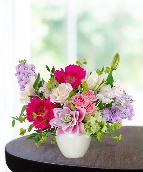 Pink Carats floral arrangement featuring pink roses, gerbera daisies, lilies, hydrangeas, and spring blooms in an ivory vase – an April birthday exclusive.