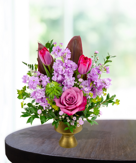 A stunning everyday flower arrangement featuring magenta roses, pink tulips, lavender stock, and a cymbidium orchid in a gold pedestal vase.