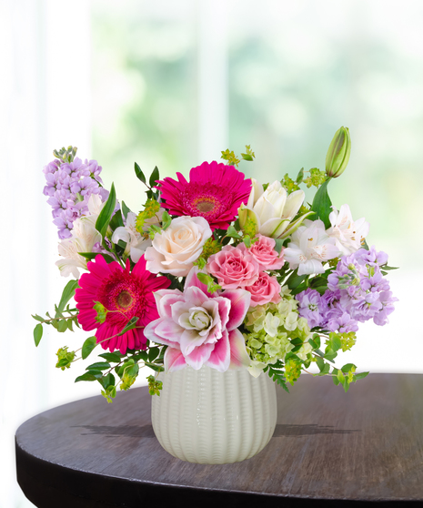 Pink Carats floral arrangement featuring pink roses, gerbera daisies, lilies, hydrangeas, and spring blooms in an ivory vase – an April birthday exclusive.