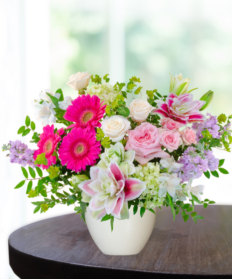 Pink Carats floral arrangement featuring pink roses, gerbera daisies, lilies, hydrangeas, and spring blooms in an ivory vase – an April birthday exclusive.