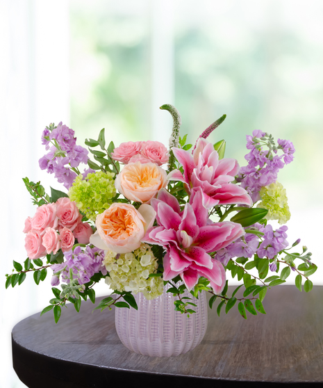 Spellbound flower arrangement with pink rose lilies, peach garden roses, pink spray roses, lavender stock, and green hydrangea in a soft blush vase