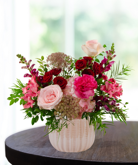 Vibrant floral arrangement featuring cranberry and blush roses in a textured cream vase for a January birthday gift.