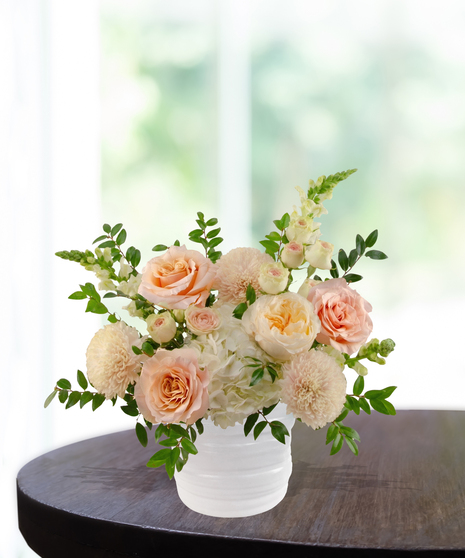 She's A Peach exclusive April birthday flower arrangement with peach garden roses, cream spray roses, white hydrangeas, and snapdragons in a ridged white vase.