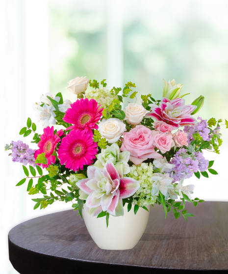 Pink Carats floral arrangement featuring pink roses, gerbera daisies, lilies, hydrangeas, and spring blooms in an ivory vase – an April birthday exclusive.