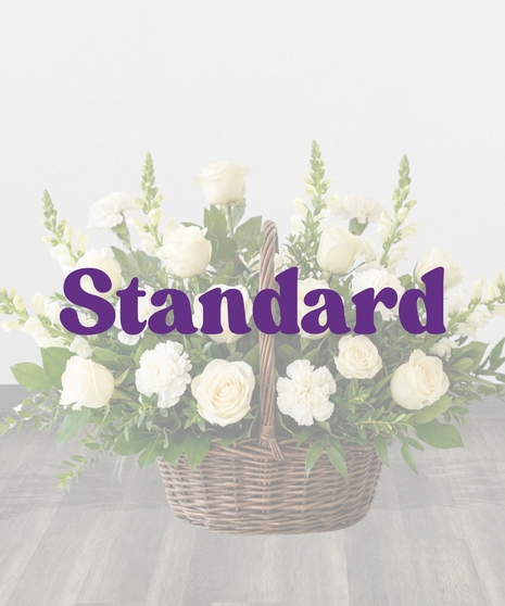 Purity Basket white sympathy flower arrangement featuring white roses, white carnations, white snapdragons, and lush green foliage in an 8-inch dark woven basket with a handle
