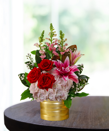 Queen of Hearts exclusive Valentine's flower arrangement with red roses, pink lilies, pink hydrangeas, pink snapdragons, and spray roses in a ribbed gold metallic vase.