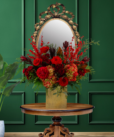 Rouge luxury Christmas flower arrangement with deep red roses, red hypericum berries, dark red foliage, and green accents in a gold vase