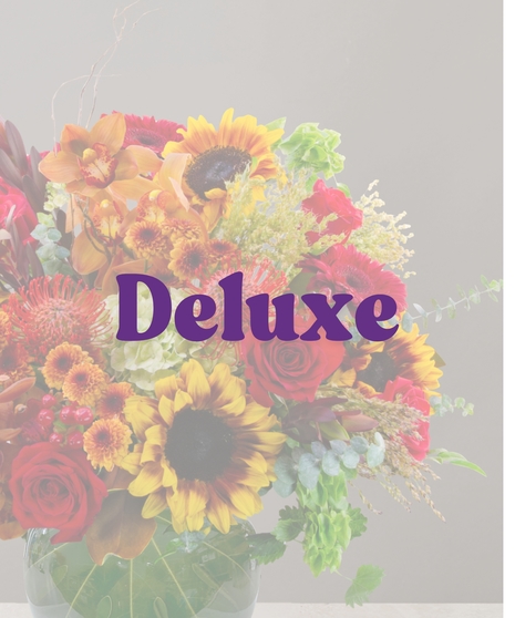 Saffron flower arrangement with sunflowers, cymbidium orchids, red roses, protea, and fall accents in a round green glass vase.