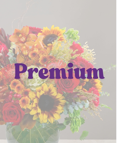 Saffron flower arrangement with sunflowers, cymbidium orchids, red roses, protea, and fall accents in a round green glass vase.