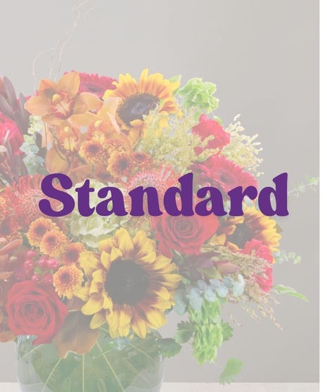 Saffron flower arrangement with sunflowers, cymbidium orchids, red roses, protea, and fall accents in a round green glass vase.