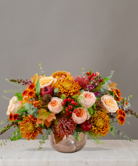 Sienna fall flower centerpiece with peach roses, gold mums, berries, pinecones, and candles in a textured vase