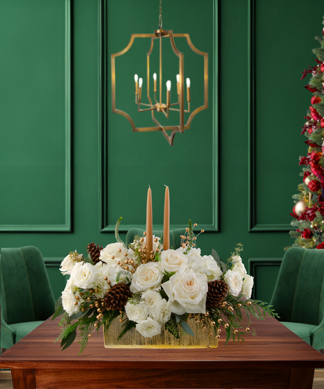 White Tie Winter elegant Christmas centerpiece with white roses, white hydrangeas, gold berries, pine cones, evergreen, and two candles in a gold rectangular vase