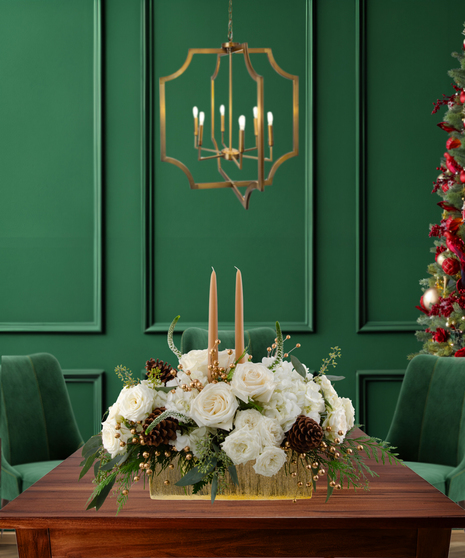 White Tie Winter elegant Christmas centerpiece with white roses, white hydrangeas, gold berries, pine cones, evergreen, and two candles in a gold rectangular vase