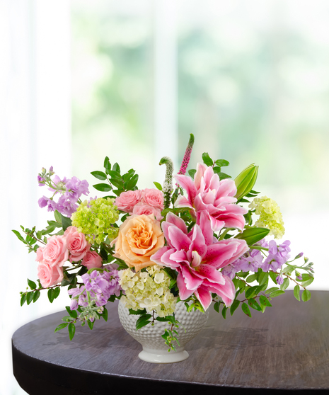 Splash of Spring March birthday arrangement featuring pink lilies, peach roses, purple stock, green hydrangeas, and tall veronica in a blue and white marbled ceramic vase