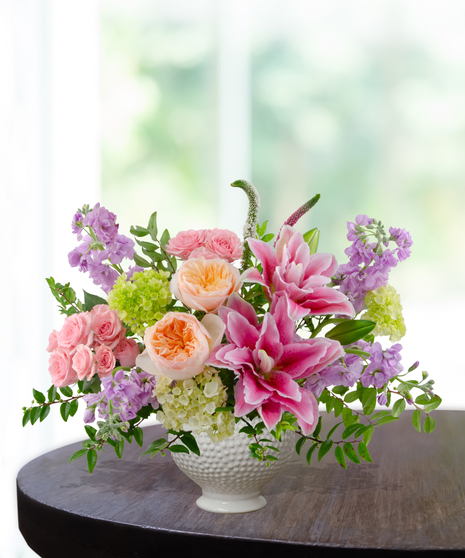 Splash of Spring March birthday arrangement featuring pink lilies, peach roses, purple stock, green hydrangeas, and tall veronica in a blue and white marbled ceramic vase