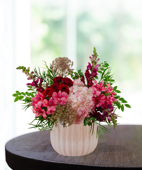 Vibrant floral arrangement featuring cranberry and blush roses in a textured cream vase for a January birthday gift.