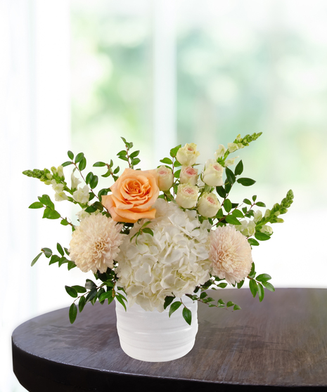 Just Peachy exclusive April birthday flower arrangement with peach garden roses, cream spray roses, white hydrangeas, and snapdragons in a ridged white vase.