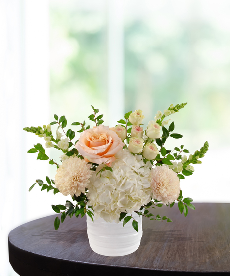 She's A Peach exclusive April birthday flower arrangement with peach garden roses, cream spray roses, white hydrangeas, and snapdragons in a ridged white vase.