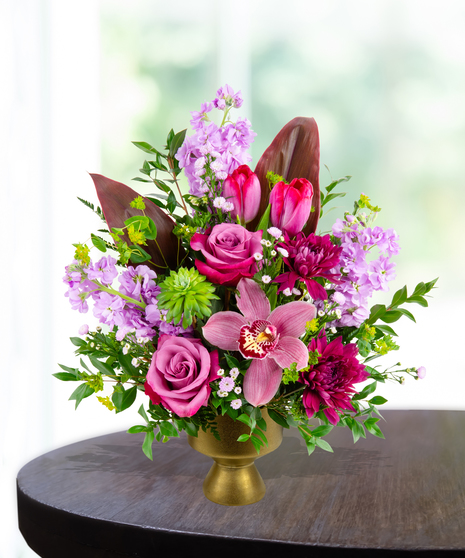A stunning everyday flower arrangement featuring magenta roses, pink tulips, lavender stock, and a cymbidium orchid in a gold pedestal vase.