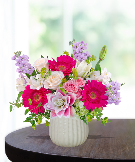 Pink Carats floral arrangement featuring pink roses, gerbera daisies, lilies, hydrangeas, and spring blooms in an ivory vase – an April birthday exclusive.