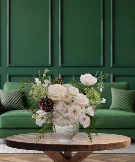 Frosted Eggnog white and green Christmas flower arrangement with white roses, white hydrangeas, green foliage, and pine cones in a textured white vase