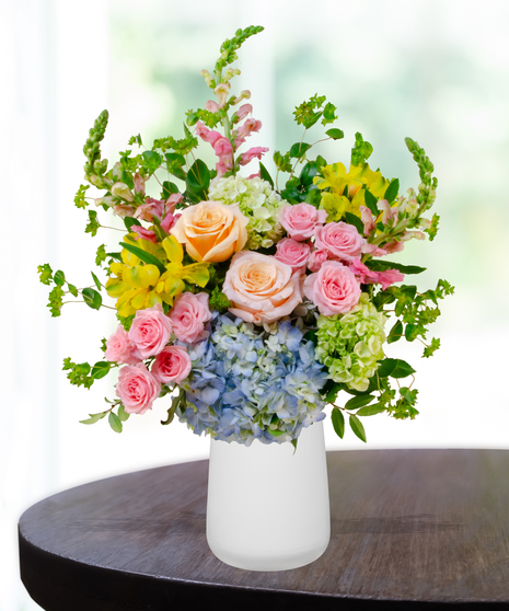 Summer Sorbet floral arrangement with peach roses, blue and green hydrangeas, yellow alstroemeria, pink spray roses, and snapdragons in a clear vase
