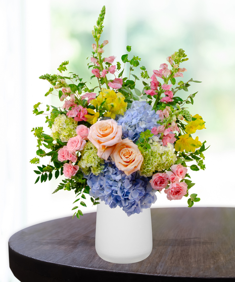 Summer Sorbet floral arrangement with peach roses, blue and green hydrangeas, yellow alstroemeria, pink spray roses, and snapdragons in a clear vase