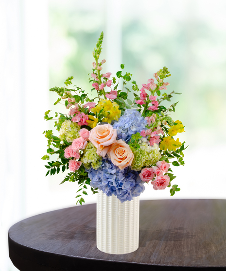 Summer Sorbet floral arrangement with peach roses, blue and green hydrangeas, yellow alstroemeria, pink spray roses, and snapdragons in a clear vase
