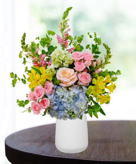 Summer Sorbet floral arrangement with peach roses, blue and green hydrangeas, yellow alstroemeria, pink spray roses, and snapdragons in a clear vase