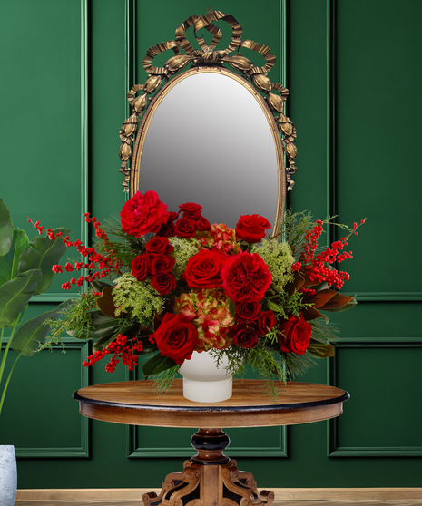 Tess Christmas flower arrangement with red roses, red hypericum berries, green hydrangea, and evergreen foliage in a white vase