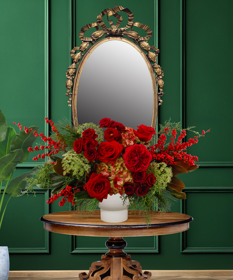 Tess Christmas flower arrangement with red roses, red hypericum berries, green hydrangea, and evergreen foliage in a white vase