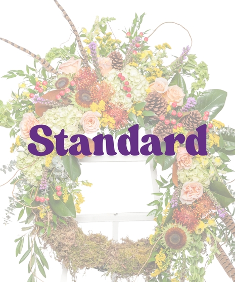 The Great Outdoors Wreath Stand with moss base, peach roses, hydrangeas, pinecones, and pheasant feathers on a white easel