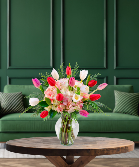 'Tis the Tulips festive Christmas bouquet with red, pink, and white tulips, pink hydrangeas, and evergreen foliage in a clear glass vase