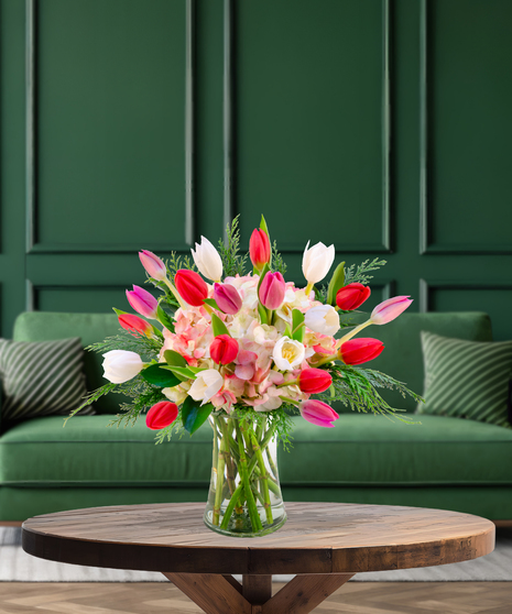 'Tis the Tulips festive Christmas bouquet with red, pink, and white tulips, pink hydrangeas, and evergreen foliage in a clear glass vase