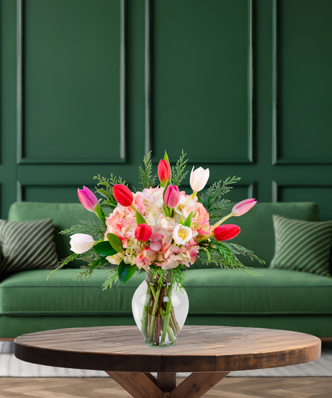 'Tis the Tulips festive Christmas bouquet with red, pink, and white tulips, pink hydrangeas, and evergreen foliage in a clear glass vase