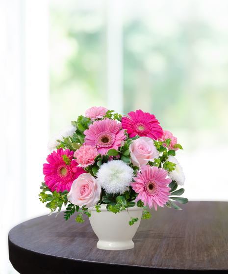 Upsy Daisy flower arrangement with hot pink gerbera daisies, pale pink roses, white mums, and carnations in a white pedestal vase.
