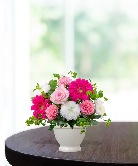Upsy Daisy flower arrangement with hot pink gerbera daisies, pale pink roses, white mums, and carnations in a white pedestal vase.
