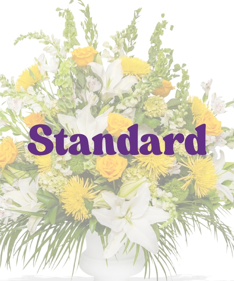 Tall pedestal urn arrangement with yellow roses, white lilies, spider mums, and tropical foliage from Billy Heroman’s in Baton Rouge
