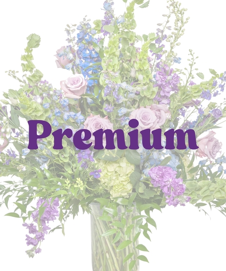 Pastel spring funeral flower arrangement in a tall glass vase with lavender roses, blue delphinium, green hydrangea, and bells of Ireland by Billy Heroman’s in Baton Rouge, LA