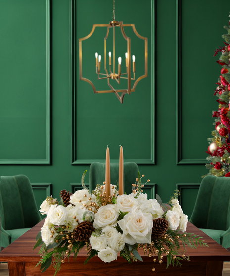 White Tie Winter elegant Christmas centerpiece with white roses, white hydrangeas, gold berries, pine cones, evergreen, and two candles in a gold rectangular vase