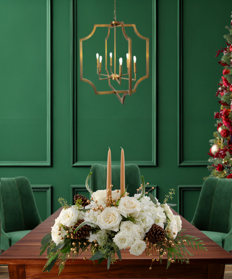 White Tie Winter elegant Christmas centerpiece with white roses, white hydrangeas, gold berries, pine cones, evergreen, and two candles in a gold rectangular vase