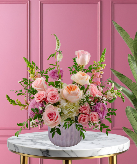 Wild About You stunning Valentine's arrangement with peach garden roses, pink roses, white hydrangeas, and pink snapdragons in a lavender ribbed vase.