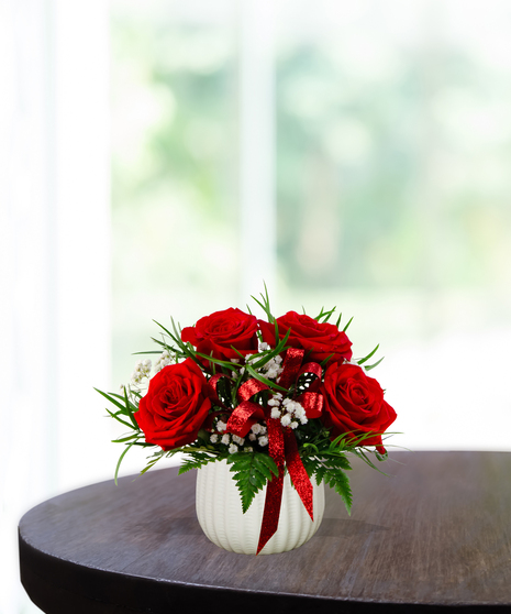 Put A Bow On It floral arrangement featuring lush red roses, white baby's breath, green foliage, and a sparkling red bow in a white ribbed vase